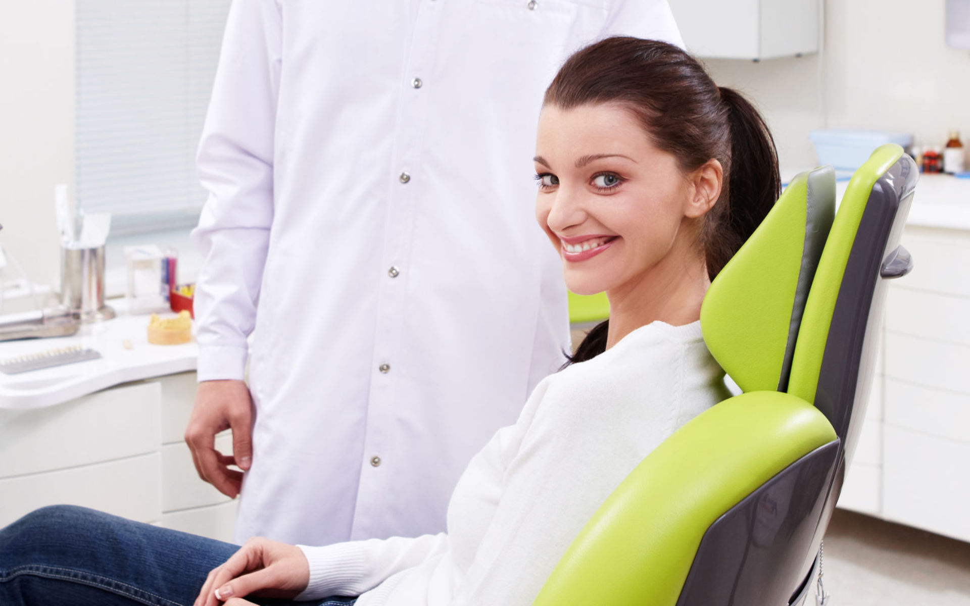 A dentist and a smiling woman sitting in a dental chair.