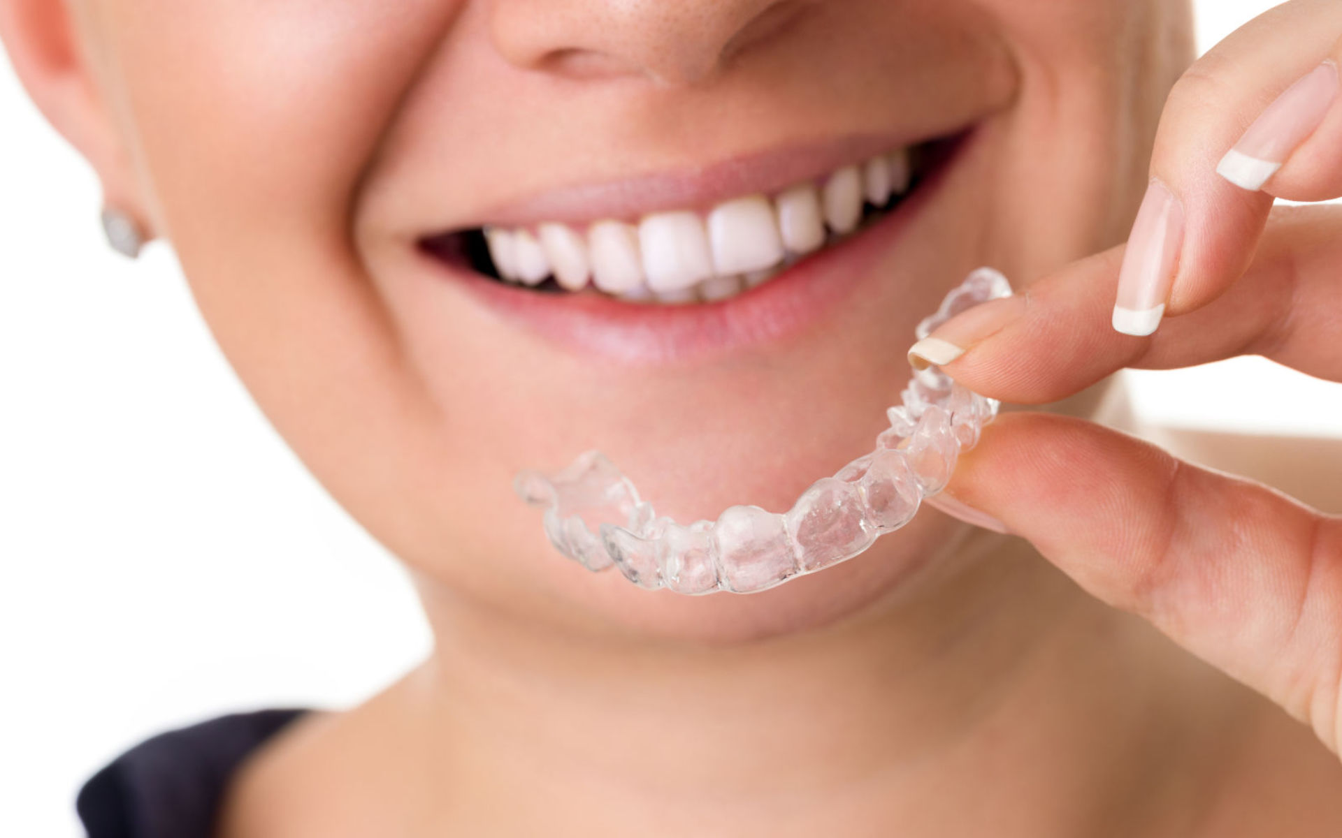 A happy woman with a perfect smile holding an invisible orthodontic aligner.